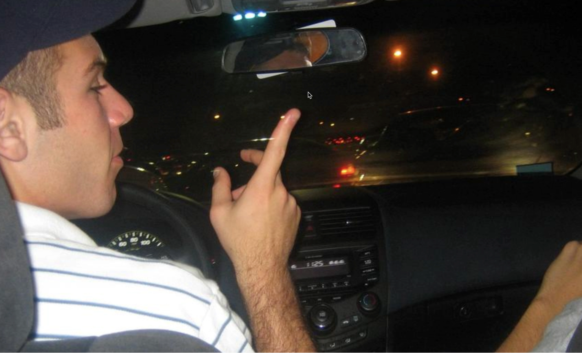 A screenshot from www.pointerpointer.com. In the image, a man in the driver seat of a car points up and to the right. Their index finger is pointing to the location of a mouse cursor.